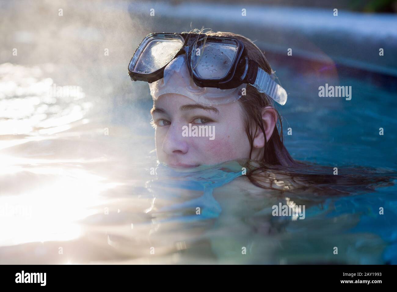 A teenage girl in a swimming pool wearing goggles, steam rising Stock