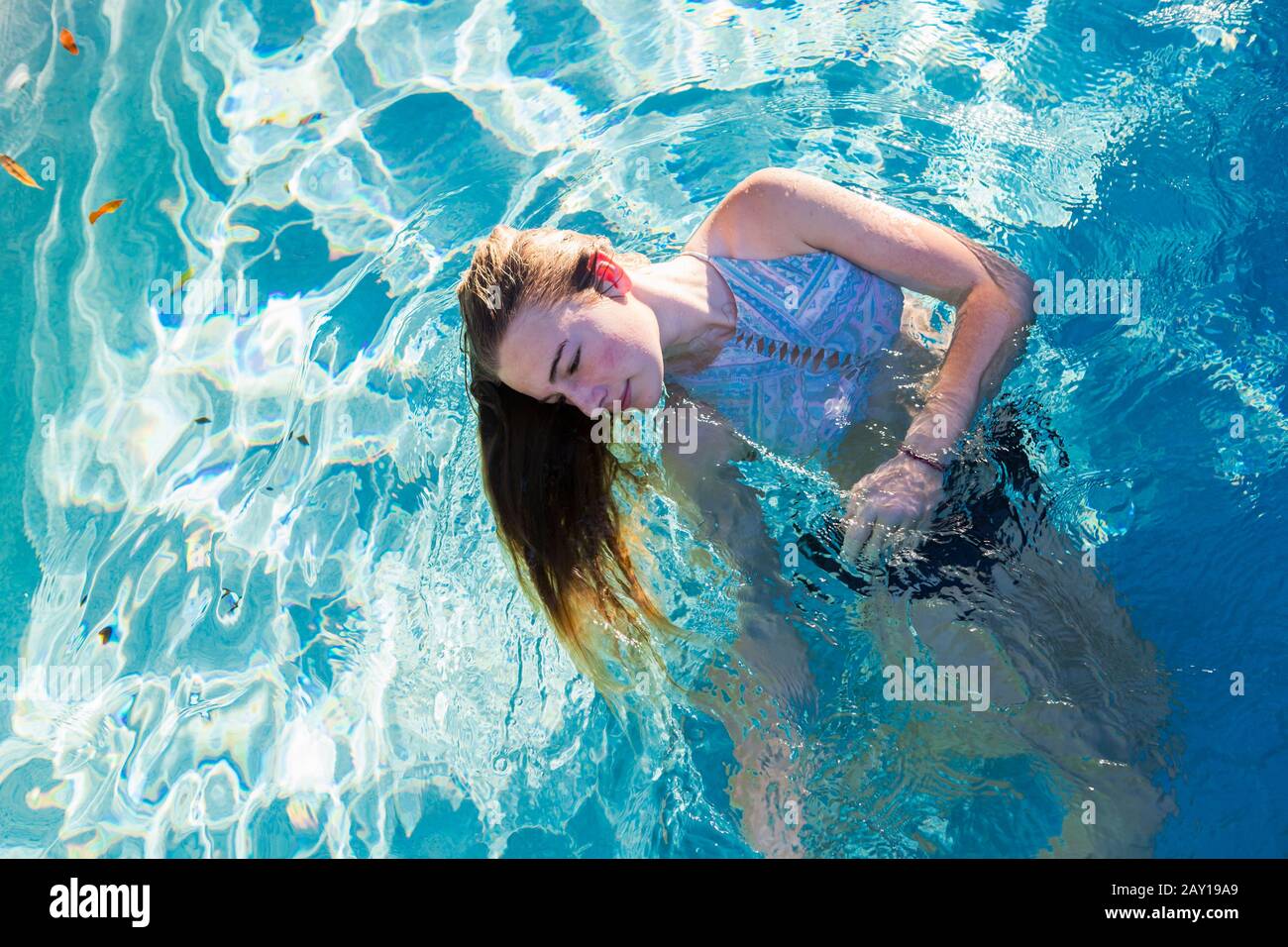A teenage girl swimming in a pool, head back hair floating in the water. Stock Photo