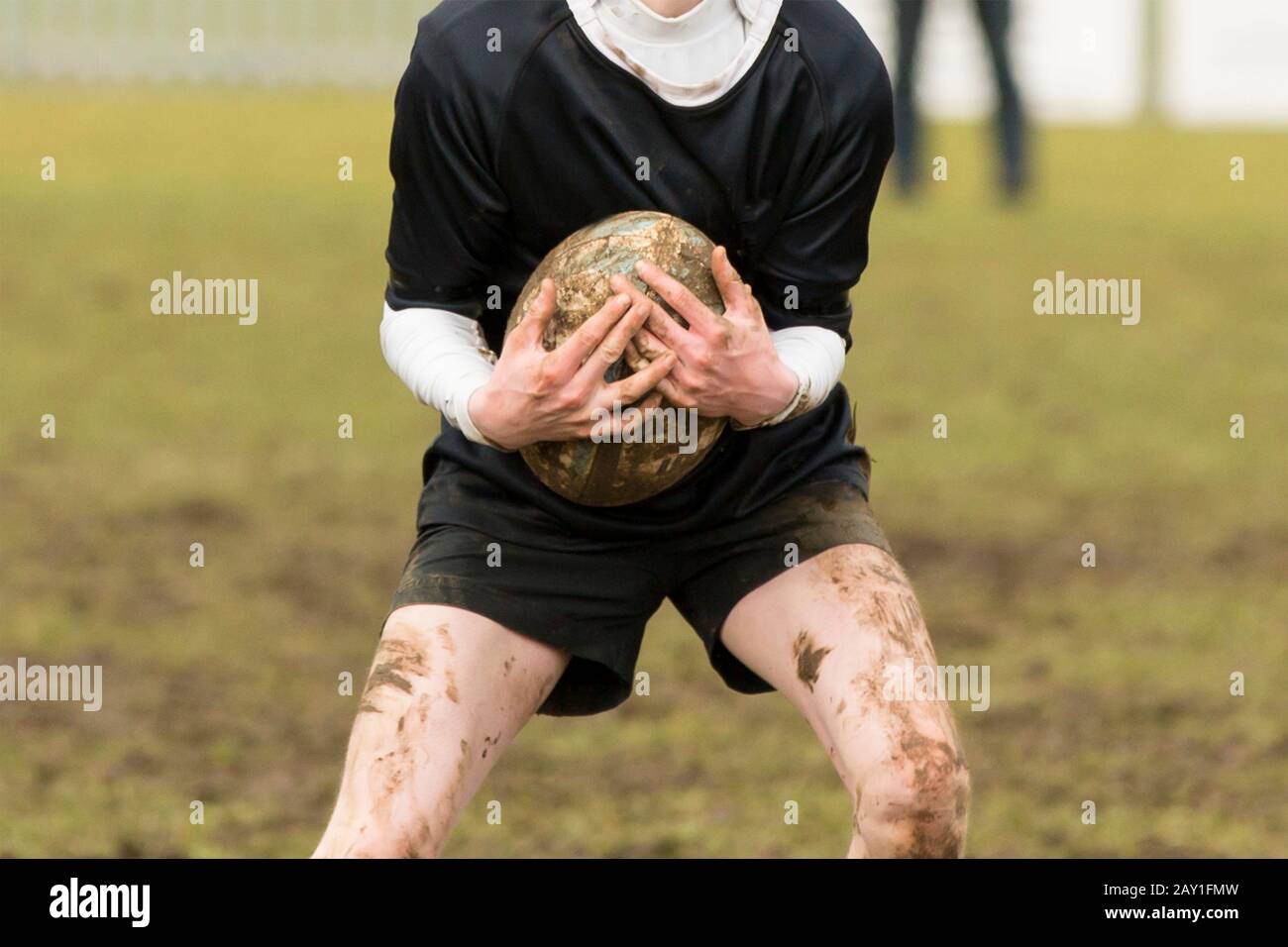 Hands holding a rugby ball during an extremely muddy rugby match. Stock Photo