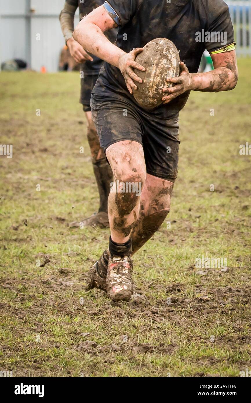 Hands holding a rugby ball during an extremely muddy rugby match. Stock Photo