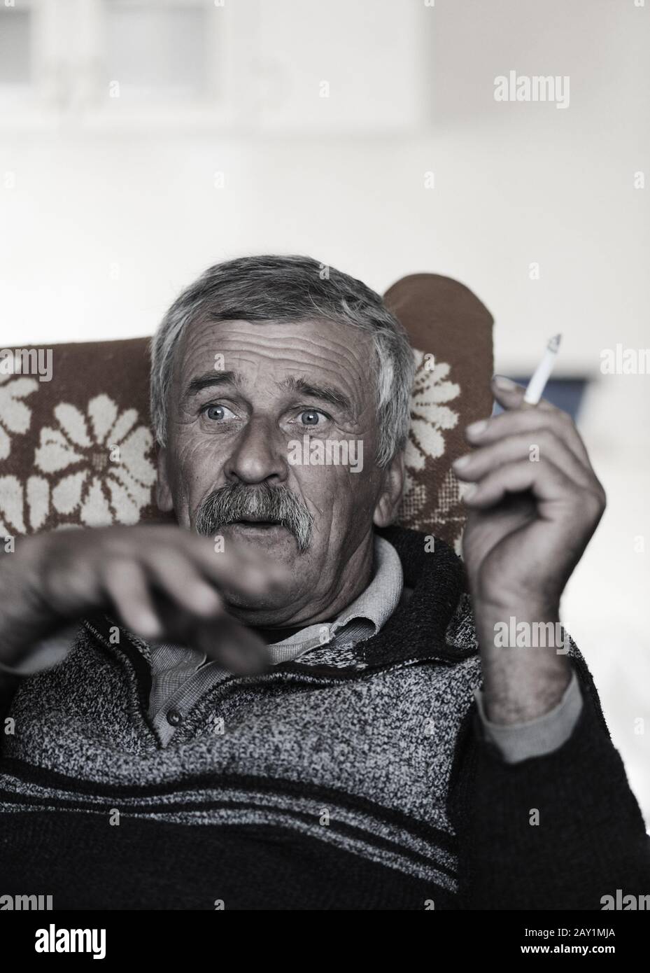 Old man with mustache smoking cigarette while sitting in sofa and speaking Stock Photo
