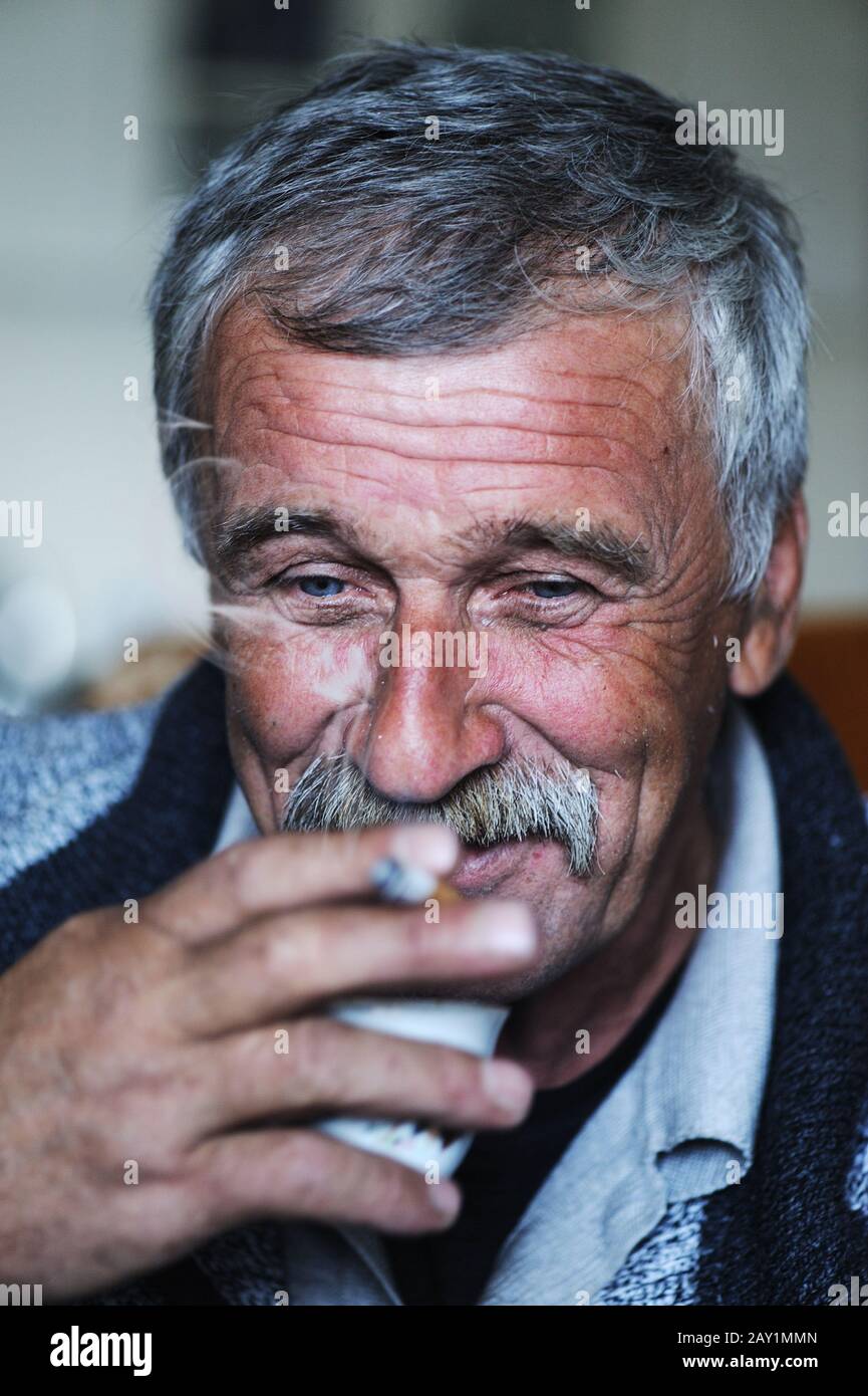 Common elderly man with mustache smoking cigarette and drinking coffee Stock Photo