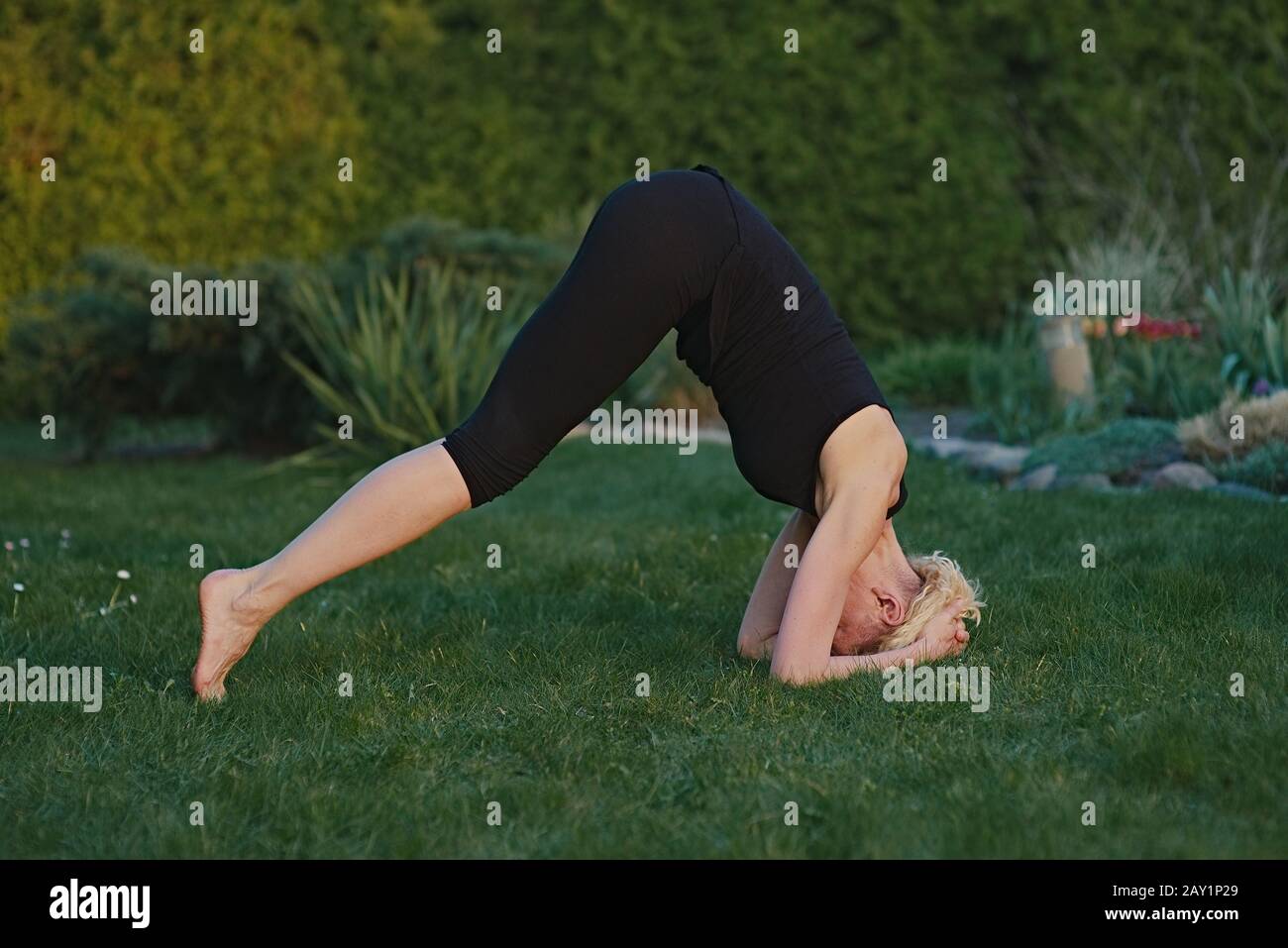 Young woman doing yoga in meditation posture on a mat in the garden. Stock Photo