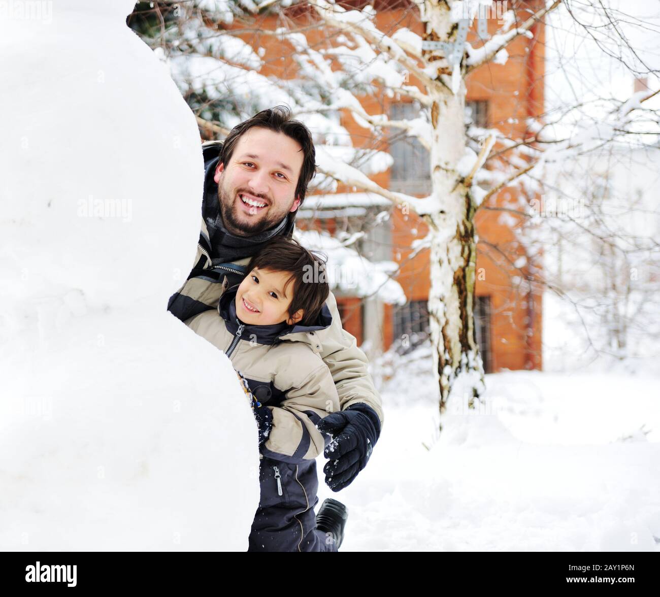 Father and son playing happily in snow making snowman, winter season