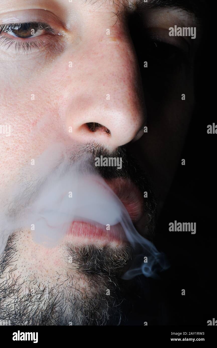 Man in dark exhaling cigarette smoke Stock Photo