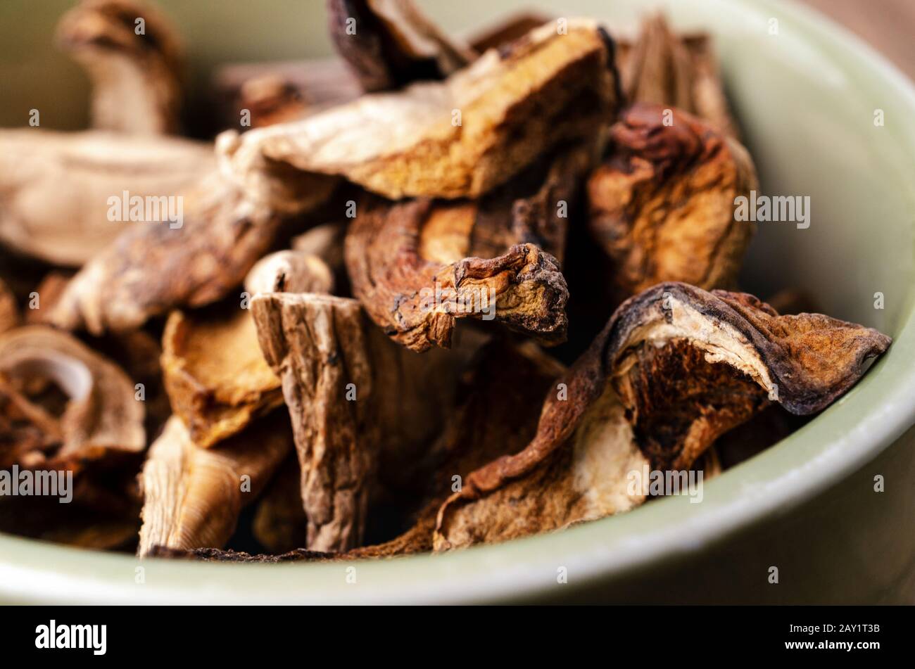Close up (macro) of dried porcini mushrooms piled up in a green ceramic bowl. Stock Photo