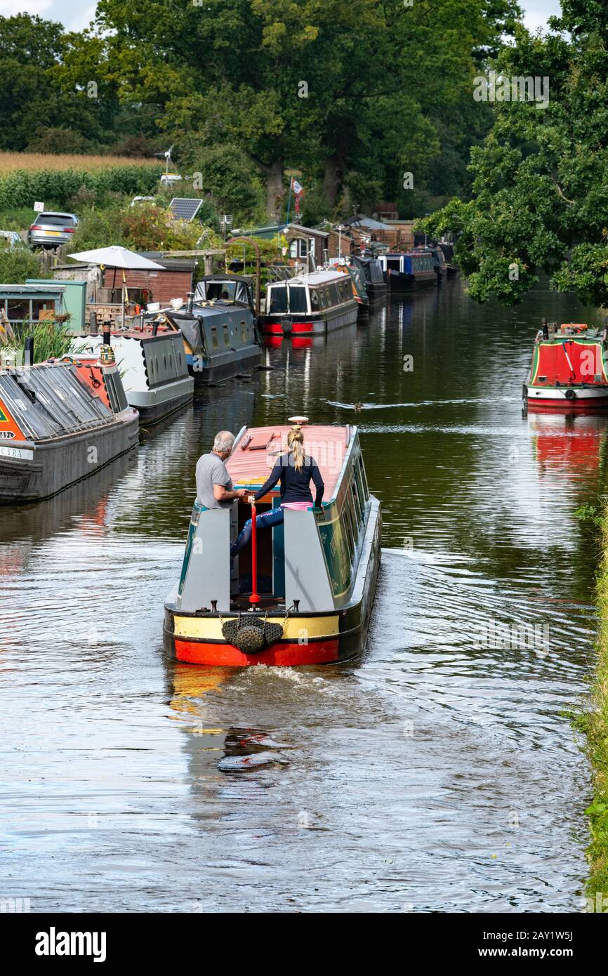 Blond-haired woman steers narrowboat long the Shroppie in Staffordshire. Stock Photo