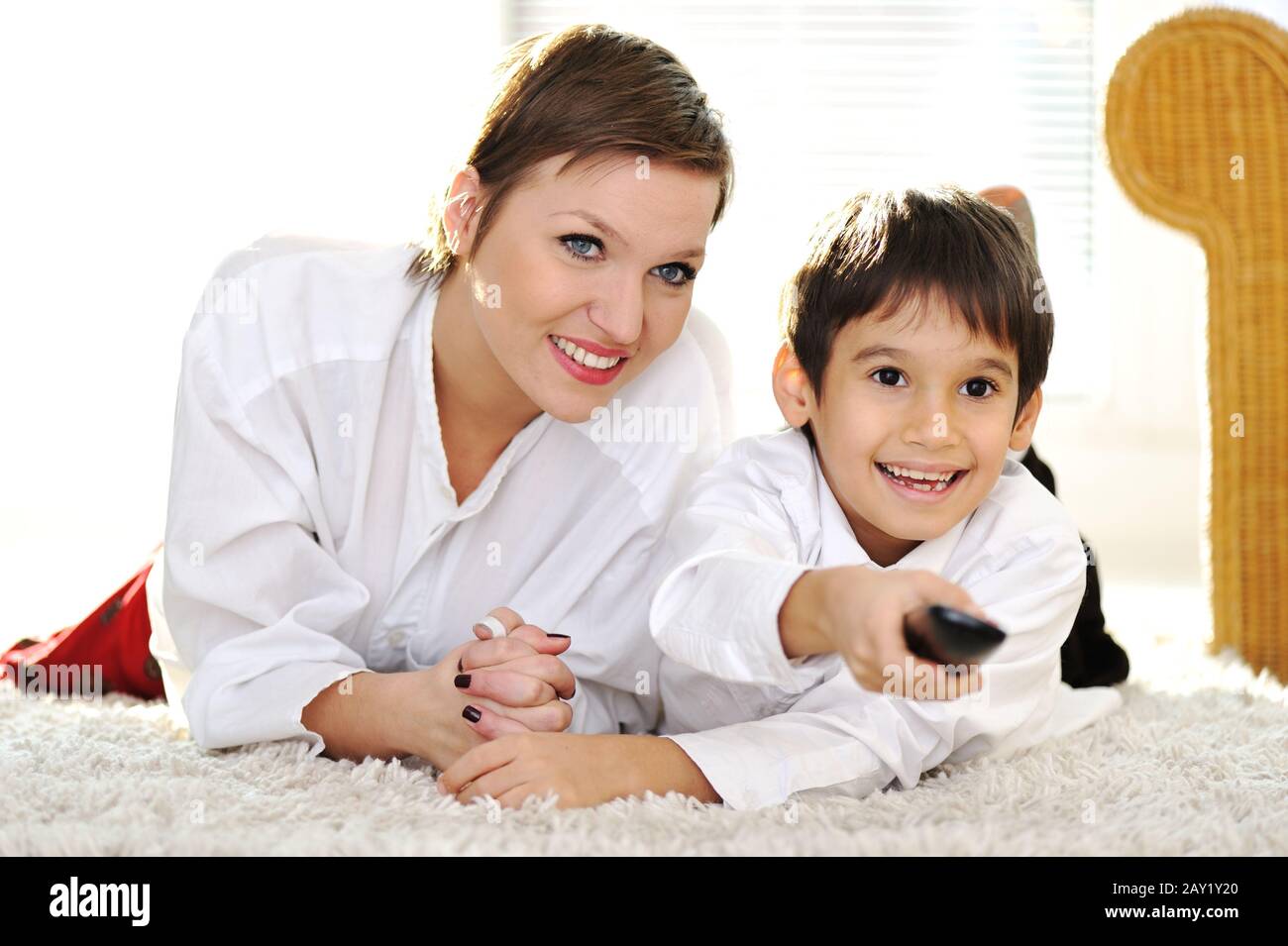Mom with son lying on floor and watching tv using remote control Stock Photo