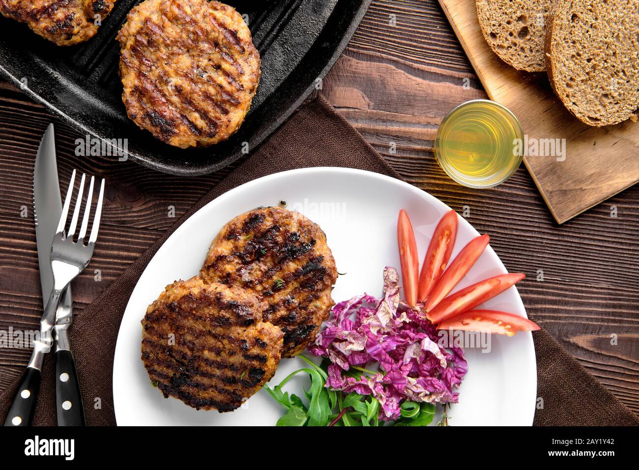 Top view of country dinner with cutlet and fresh salad, brown bread and moonshine on rustic wooden table Stock Photo