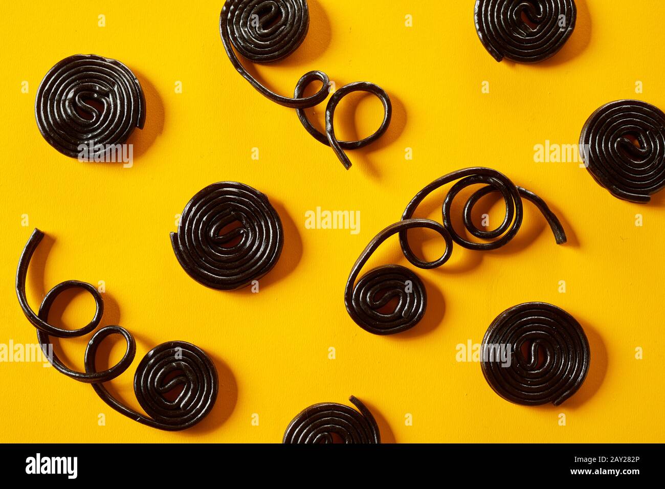 Coiled spirals of liquorice with trailing strands in a random pattern on a vivid yellow background in a full frame view Stock Photo