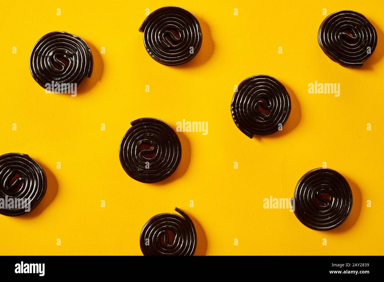 Spiral coils of fresh liquorice candy scattered on a colorful vibrant yellow background in a full frame view Stock Photo