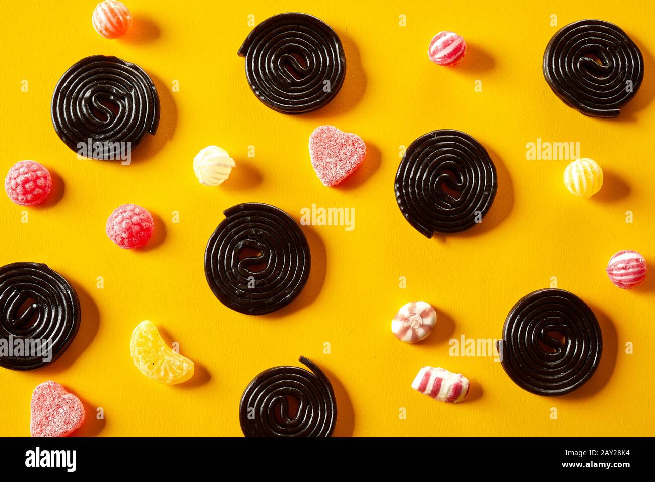 Spiral liquorice coils with fruity jub jub candy between scattered on a yellow background in a decorative pattern from overhead Stock Photo