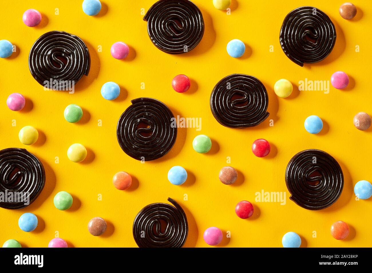 Coiled spirals of liquorice with sugar-coated chocolate candy on an exotic vibrant yellow background in a random pattern Stock Photo