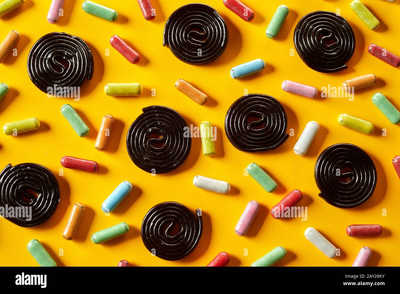 Liquorice spirals and sugar-coated candy arranged in a random pattern on an exotic yellow background in full frame view Stock Photo