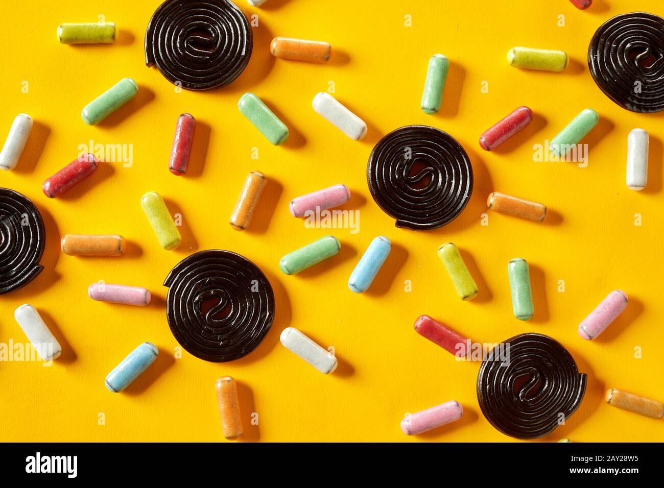 Background pattern of candy suns with spiral coiled liquorice centres and sugar-coated colorful rays on a tropical yellow background Stock Photo