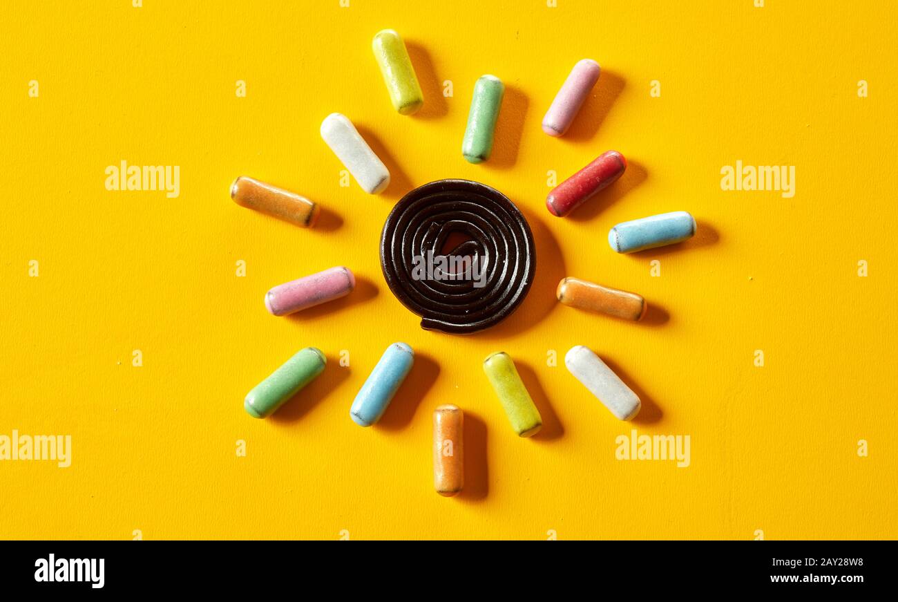Summer sun concept with colorful sugar-coated candy around a spiral coil of liquorice over a bright yellow tropical background Stock Photo