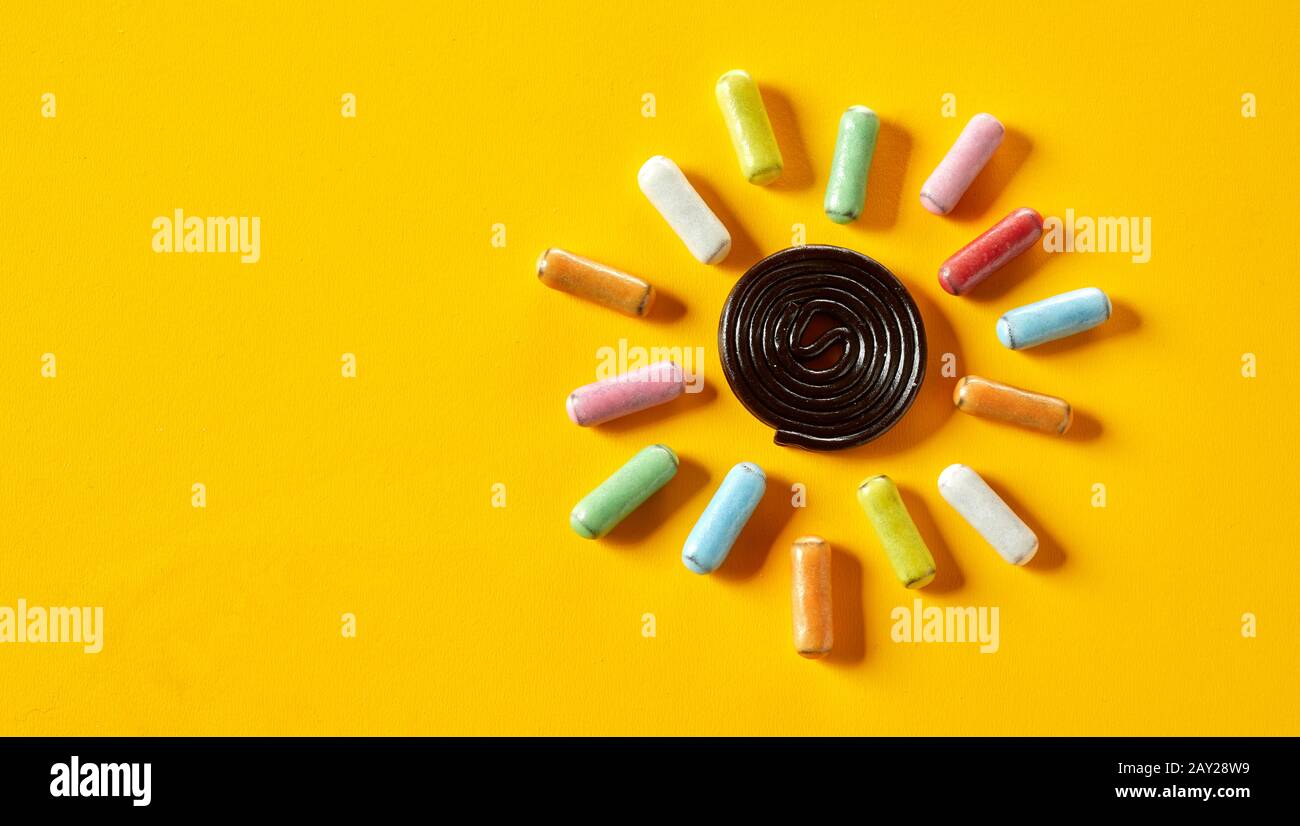 Colorful candy sun on a tropical yellow background conceptual of summer with liquorice coils and sugar-coated sweets Stock Photo