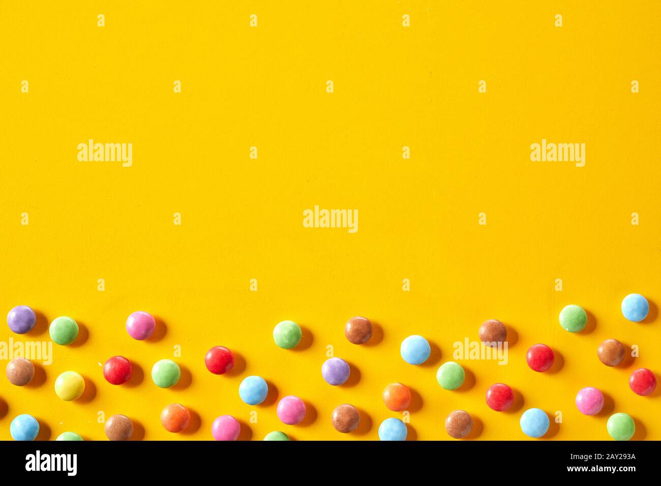 Colorful candy border with sugar-coated chocolate sweets in rainbow colors scattered over a bright yellow background with copy space Stock Photo
