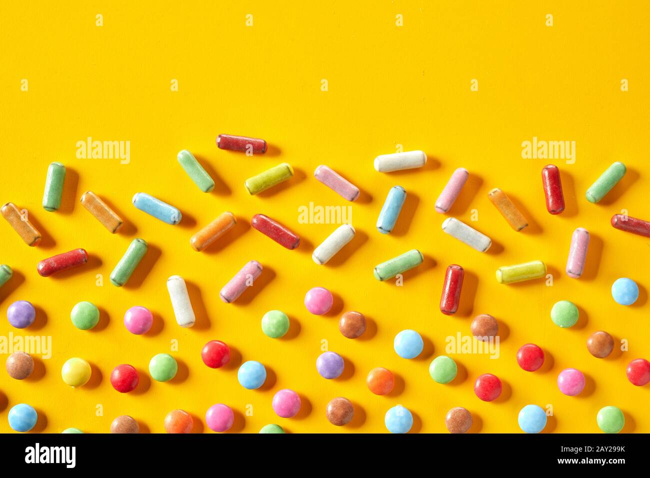 Double border of colorful sugar-coated candies with liquorice and chocolate on a yellow background with top copy space Stock Photo