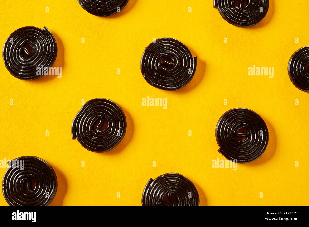 Liquorice coils on a bright yellow background arranged in diagonal rows in a full frame view Stock Photo