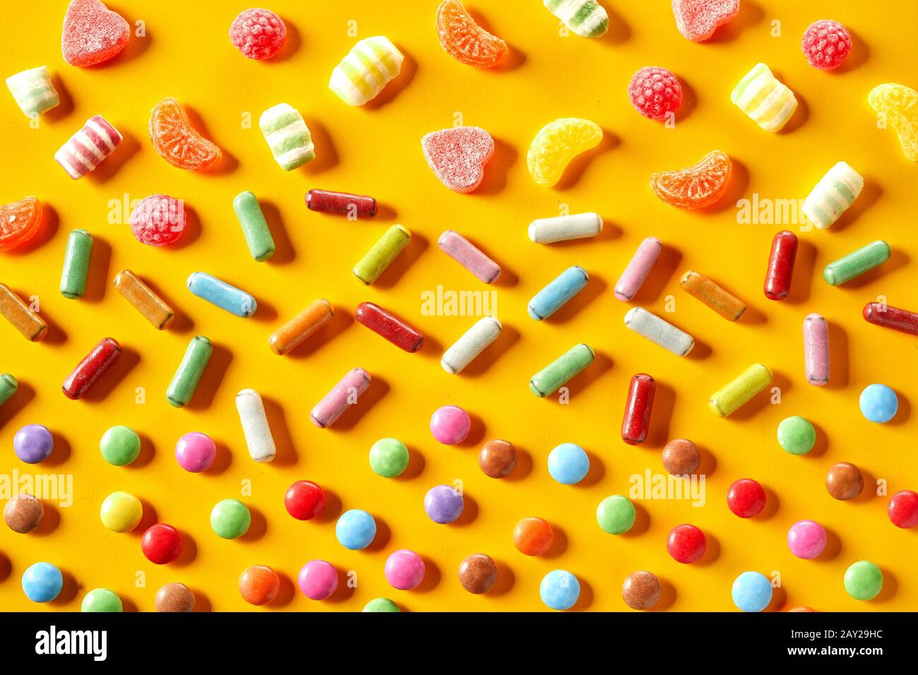 Colourful party background of rainbow candy with fruity jelly jub jubs, sugar-coated liquorice and chocolate over a vibrant yellow in a full frame vie Stock Photo