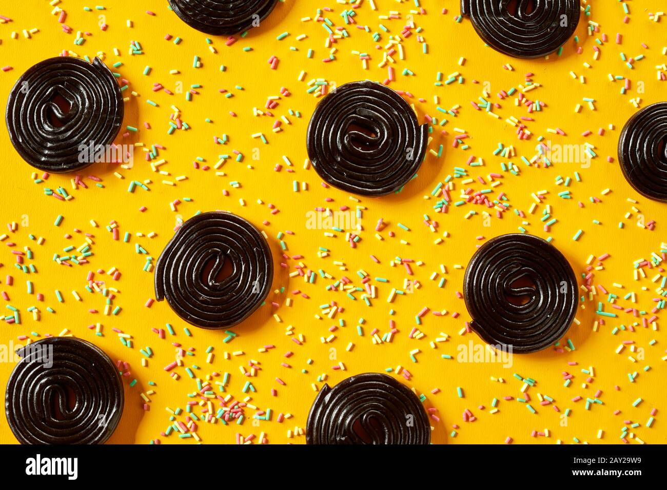Rows of spiral liquorice coils with colorful baking sprinkles background texture over a bright yellow surface in a full frame view Stock Photo
