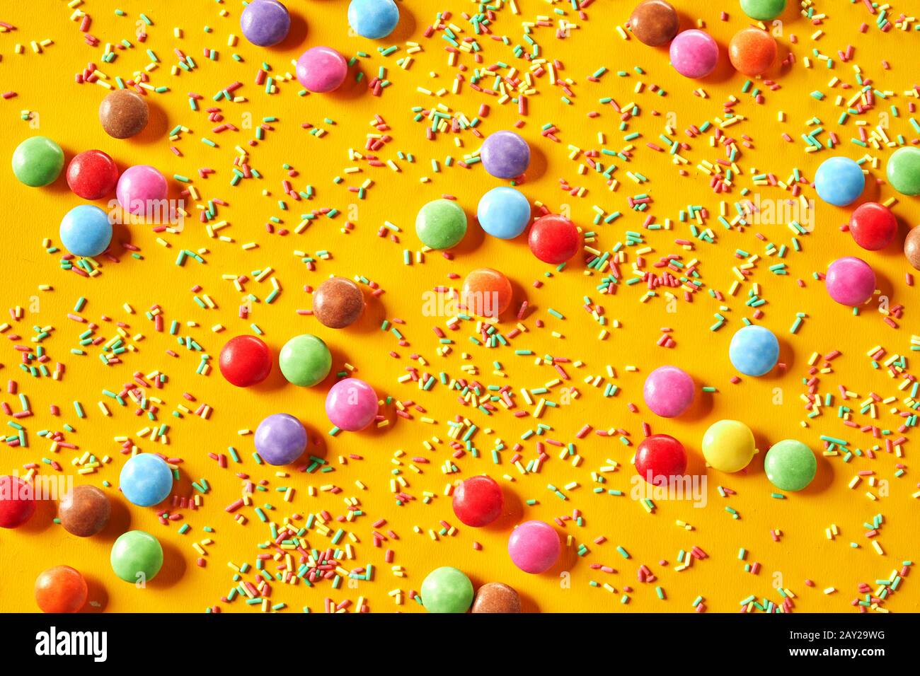 Colorful exotic party background of rainbow sugar-coated chocolate candy and sprinkles on a yellow full frame background Stock Photo