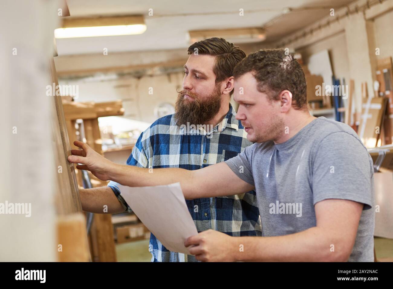 Two carpenters discuss the dimensions for a furniture order in the joinery Stock Photo