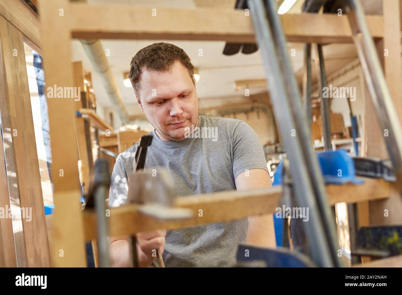 Young man as a carpenter apprentice works in the carpentry with screw clamps Stock Photo