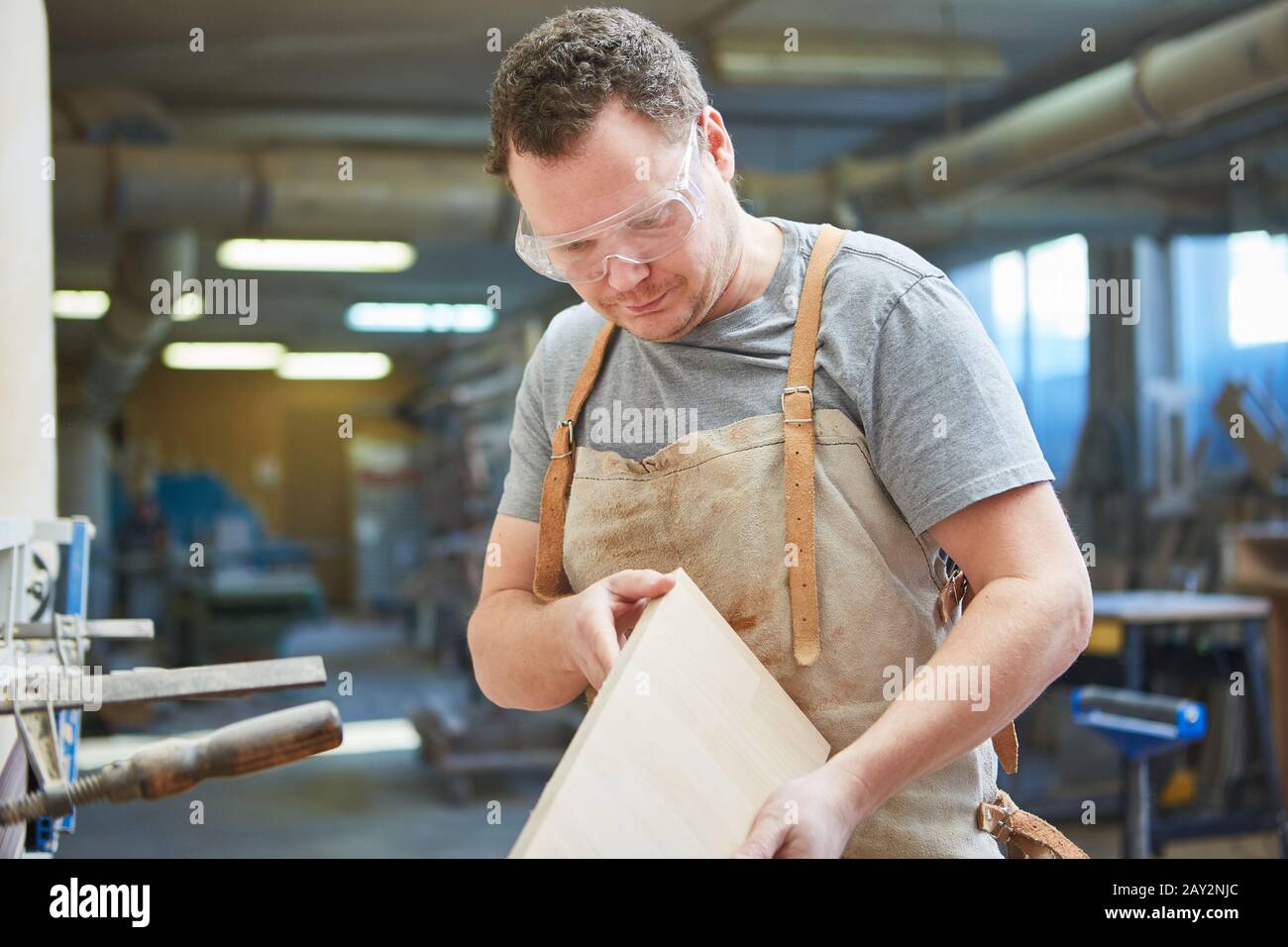 Carpenter as a furniture maker with safety glasses controls a workpiece in the carpentry Stock Photo