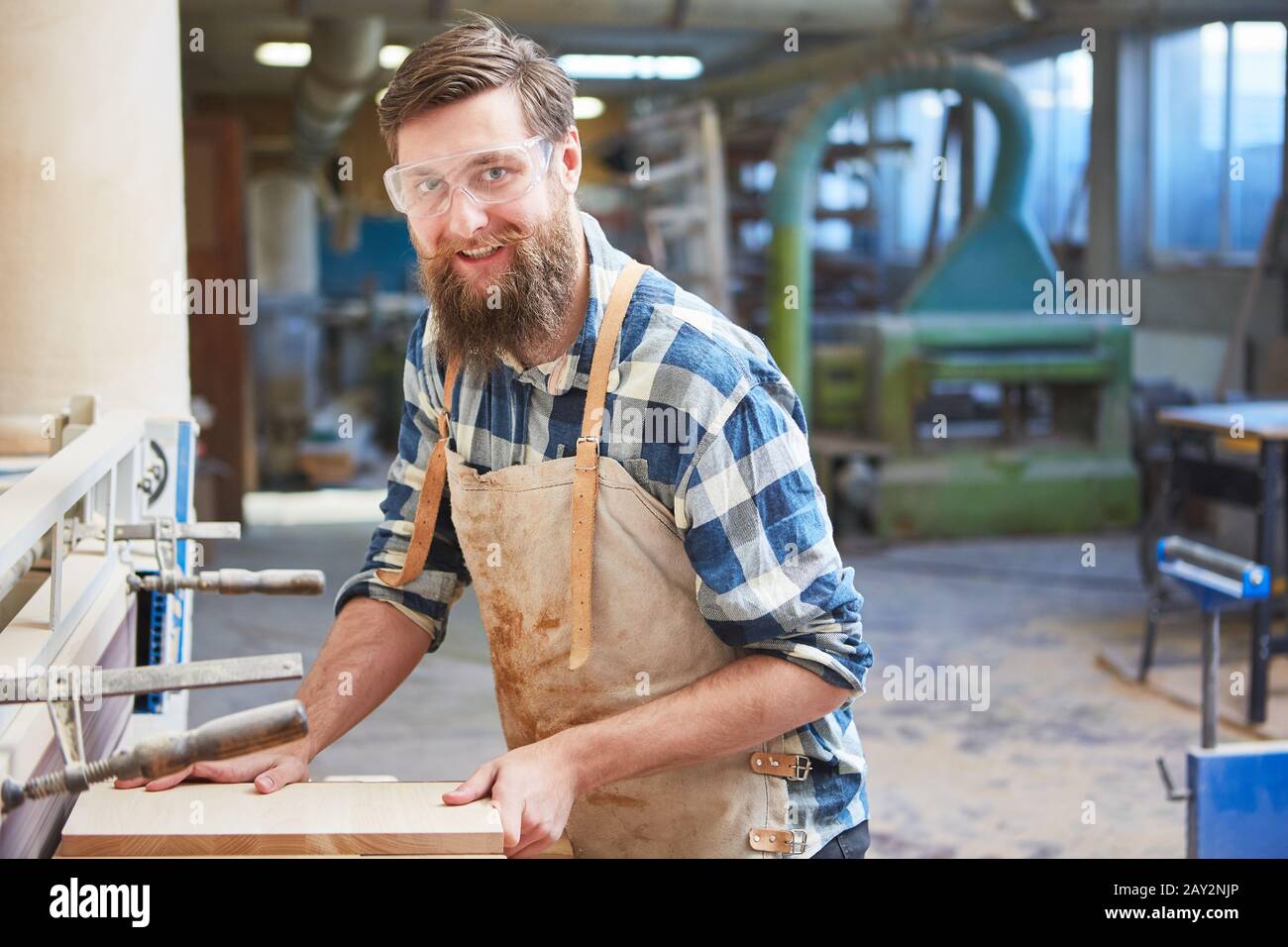 Hipster carpenter with a beard as a furniture maker works with wood on the grinding machine Stock Photo