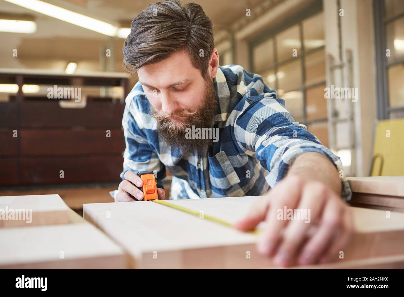 Carpenter as a furniture maker measuring wood using a tape measure in a carpenter's workshop Stock Photo
