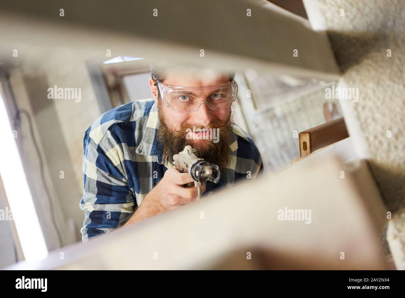 Painter using the spray gun while painting furniture with wood glaze in