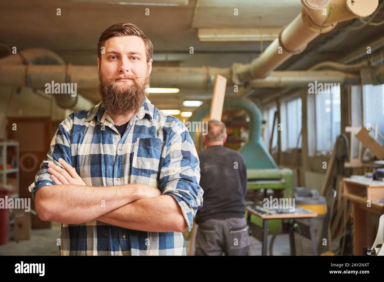 Hipster carpenter with a beard as a boss in his joinery with his arms crossed Stock Photo