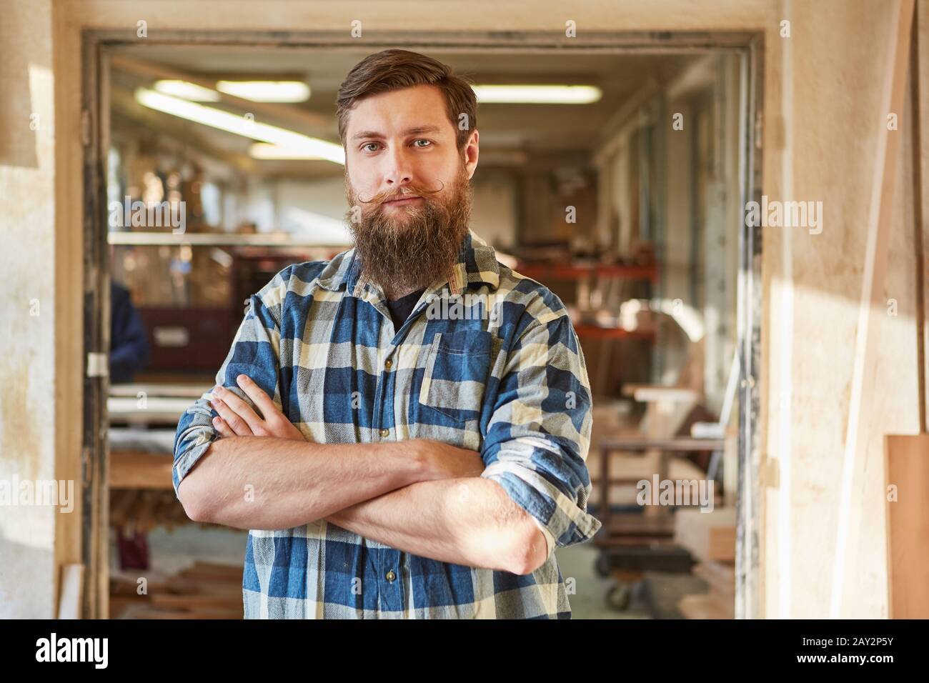 Hipster carpenter or joiner with crossed arms in a carpentry workshop Stock Photo