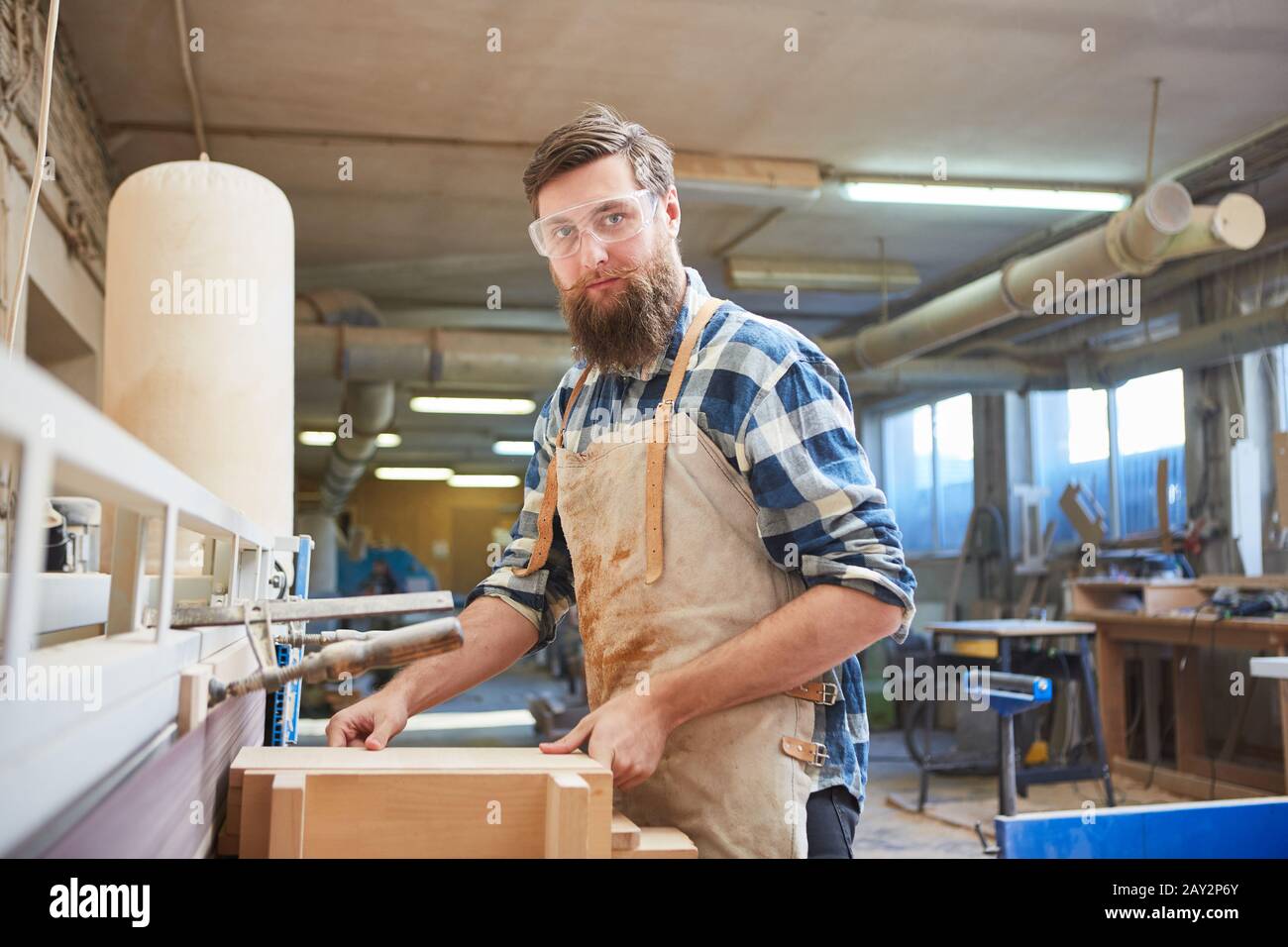 Hipster man with a beard as a furniture maker on the grinding machine in the carpentry Stock Photo