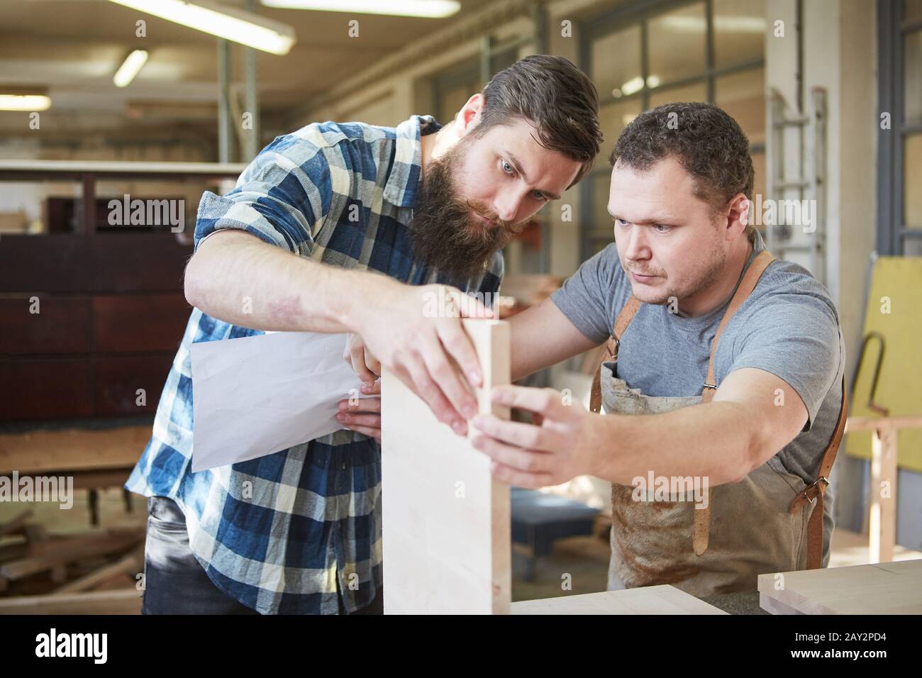 Two carpenters in training build a wooden shelf together in the joinery Stock Photo