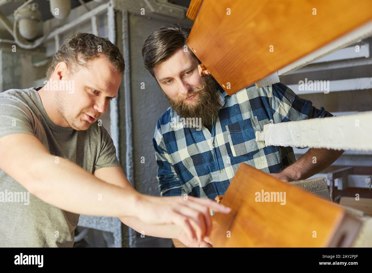 Carpenter apprentice in training and instructor discuss a wooden workpiece Stock Photo