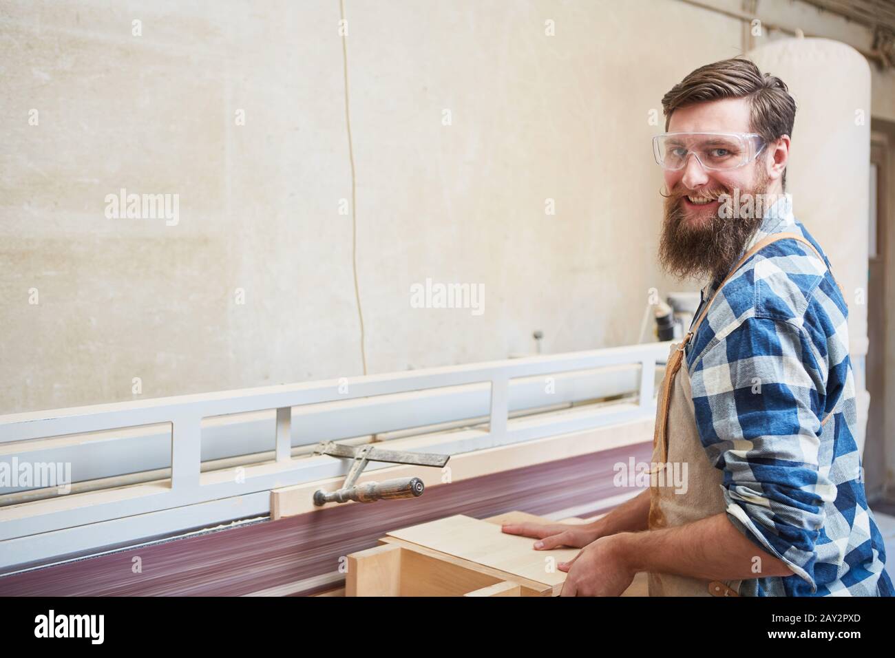 Carpenter apprentice with wood on the grinding machine during furniture construction in the workshop Stock Photo