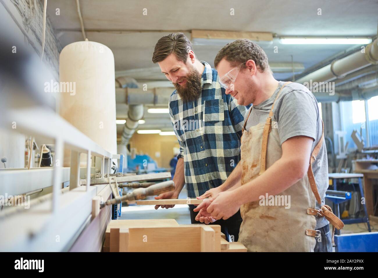 Two furniture makers with wooden furniture workpiece are working on the grinding machine Stock Photo