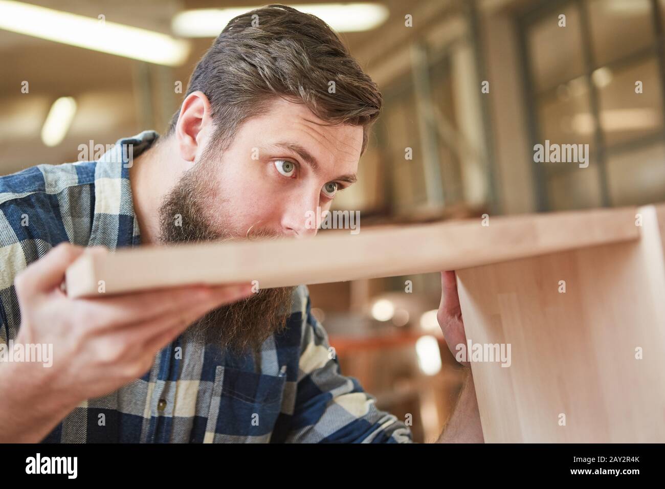 Carpenter apprentice mortises a wooden shelf in a joinery or joinery Stock Photo