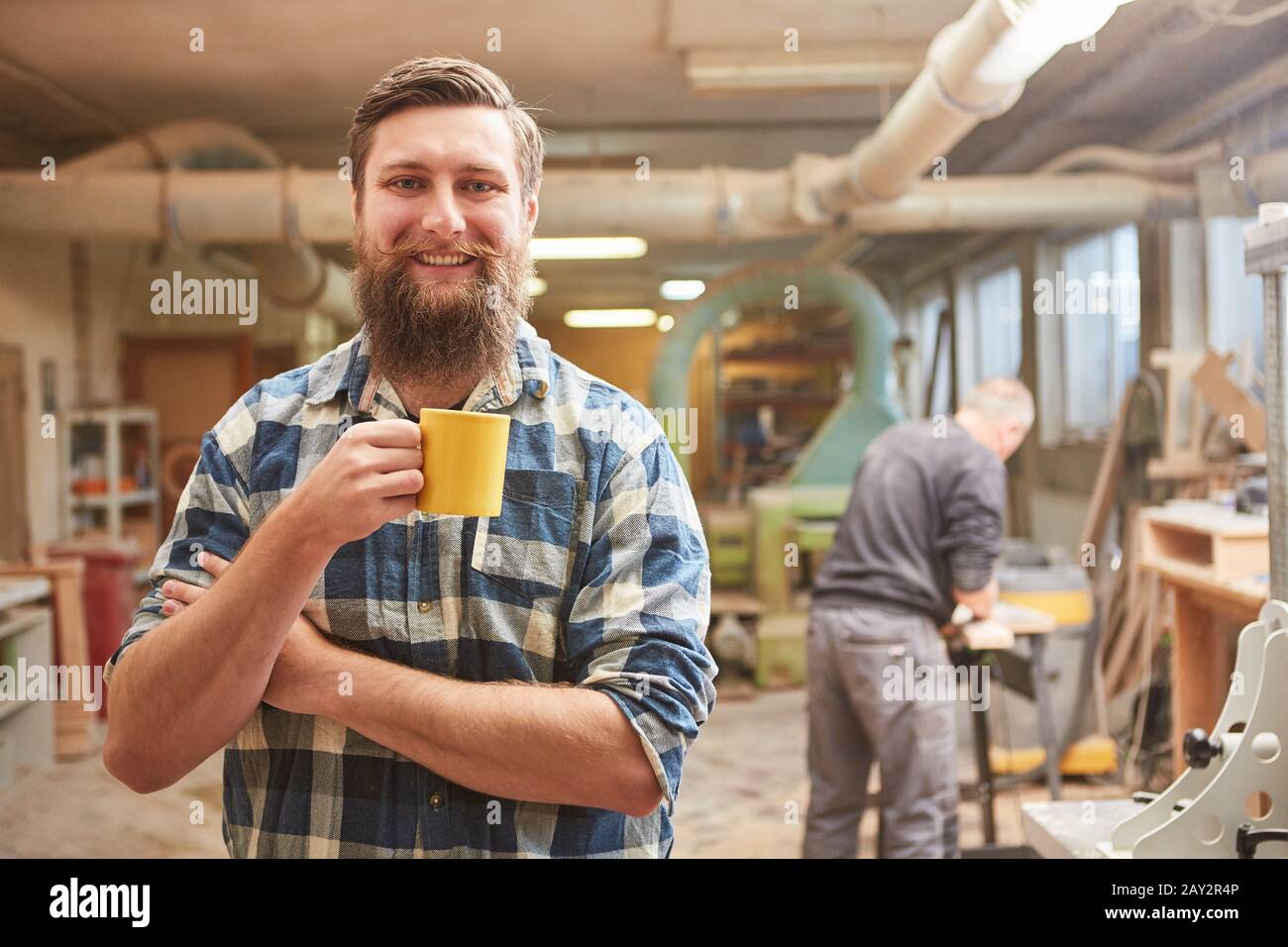 Smiling hipster carpenter with beard takes coffee break in his joinery Stock Photo