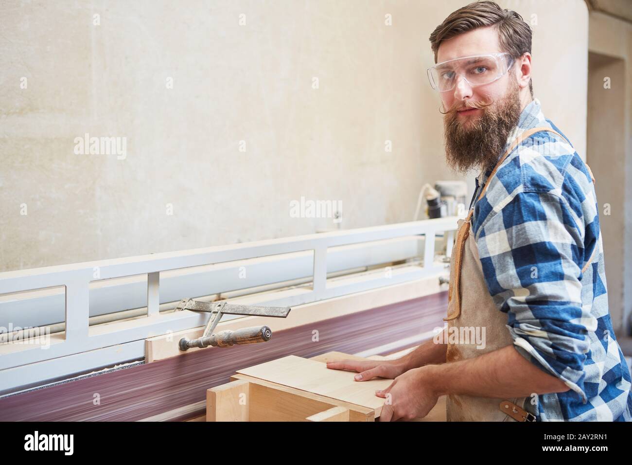 Hipster man as carpenter apprentice with wood on the grinder in the carpentry workshop Stock Photo