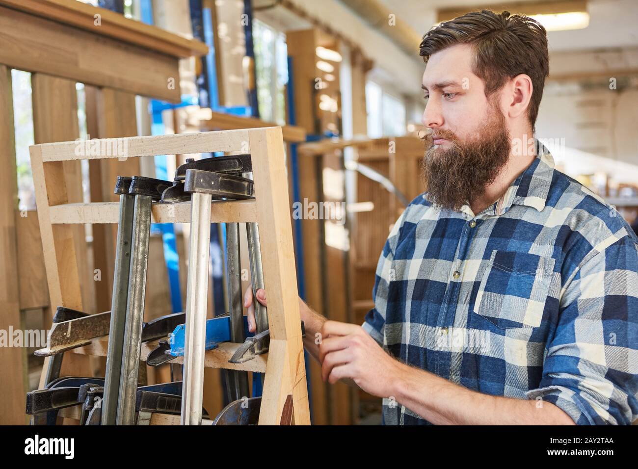 Hipster man with a beard as a carpenter or furniture maker works with clamps Stock Photo