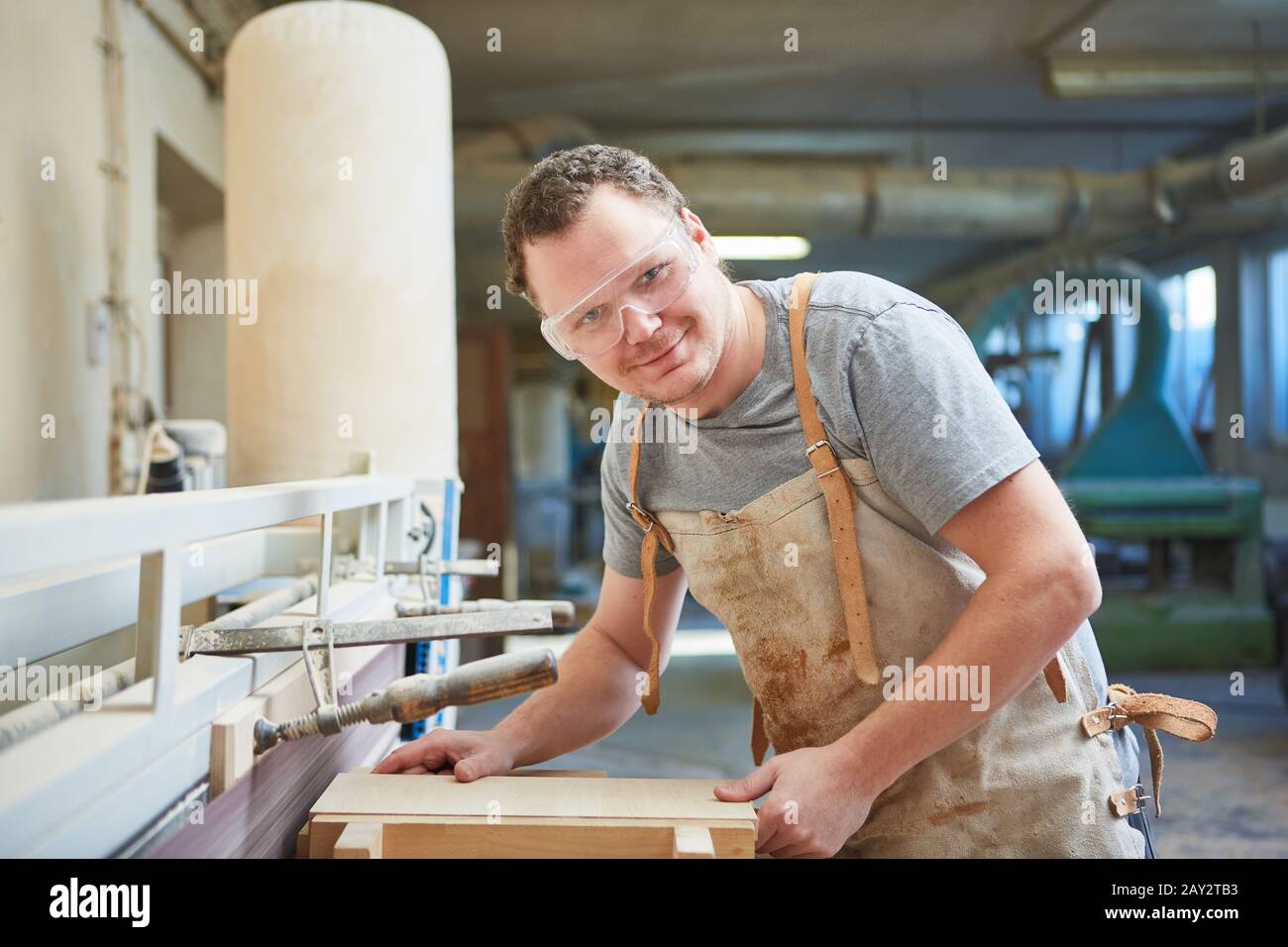 Carpenter with safety glasses works on the grinding machine with a wooden workpiece Stock Photo