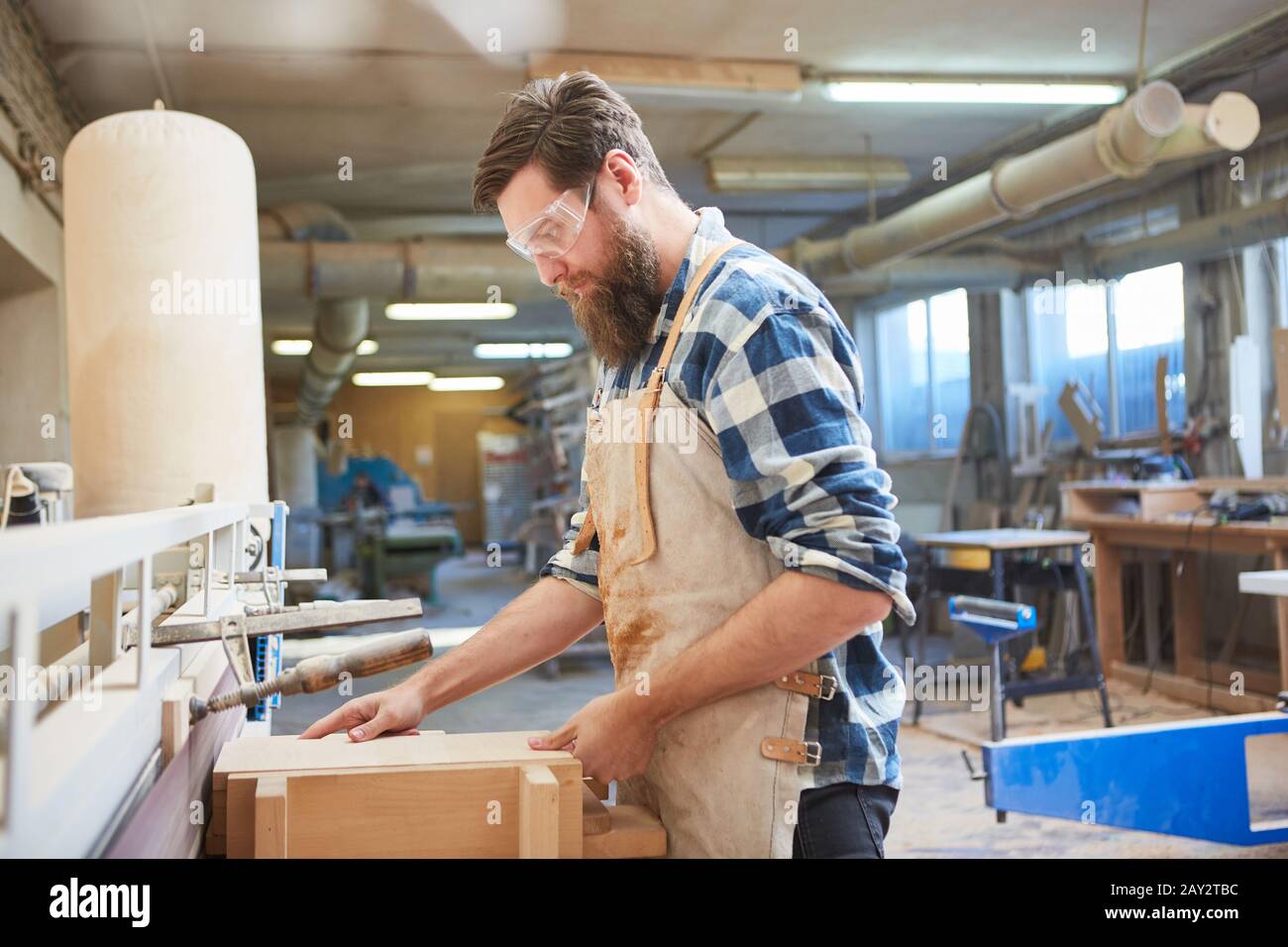 Carpenter with safety glasses on the grinding machine in the carpentry workshop Stock Photo