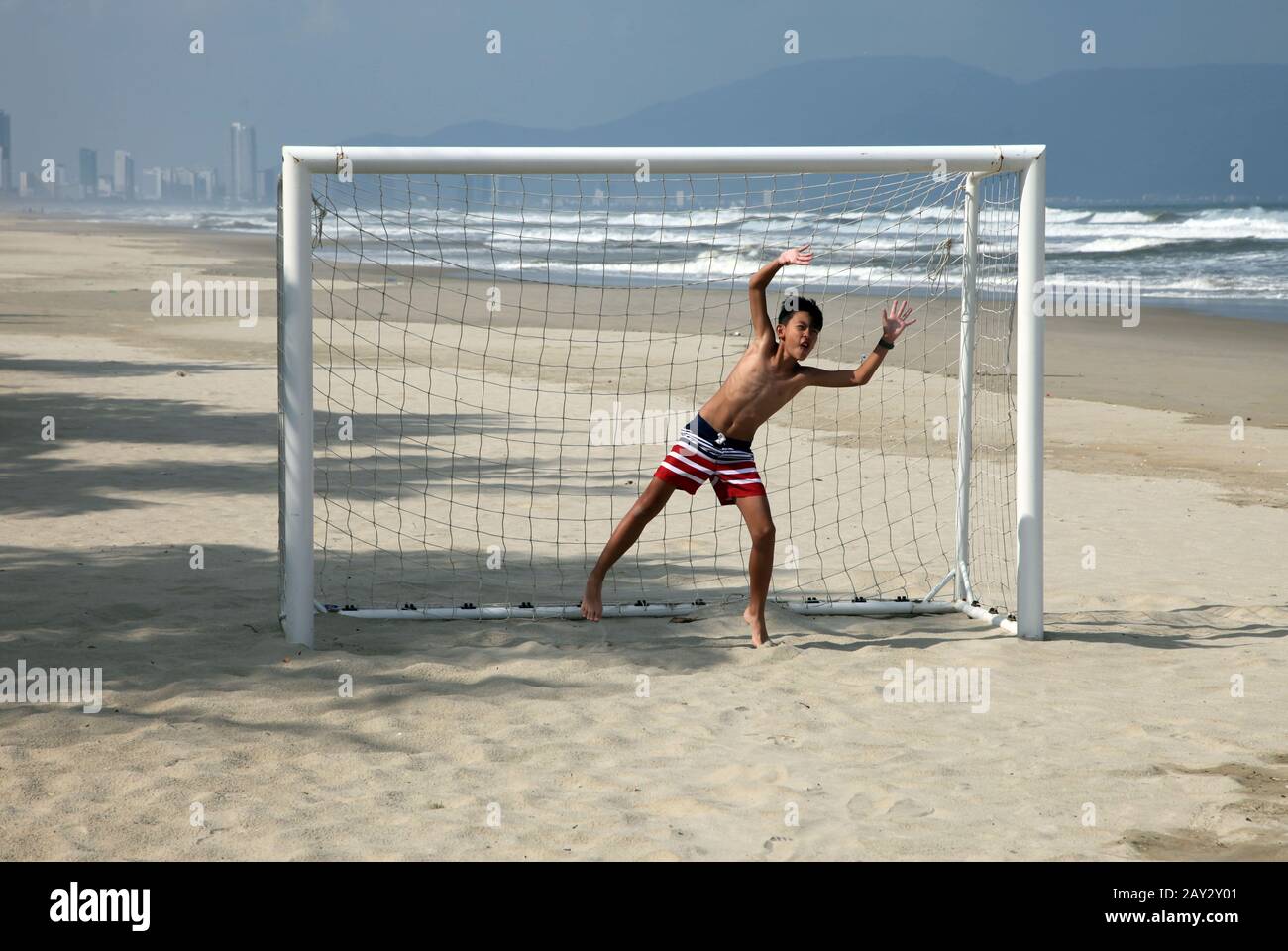 Kid goalkeeper playing on a football or soccer game on the beach Stock Photo