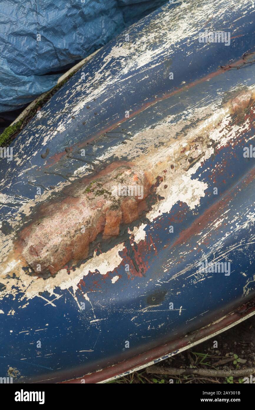 Upturned blue fibreglass hull of beached kayak, showing repaired glass fibre strands and fabric. Kayak repairs, fibreglass repairs, fibreglass texture. Stock Photo