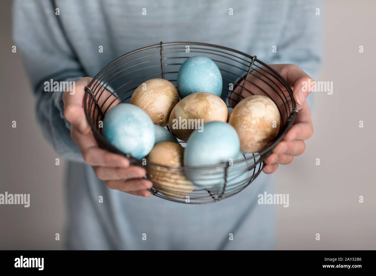 Hands holding colored eggs in wire basket Stock Photo