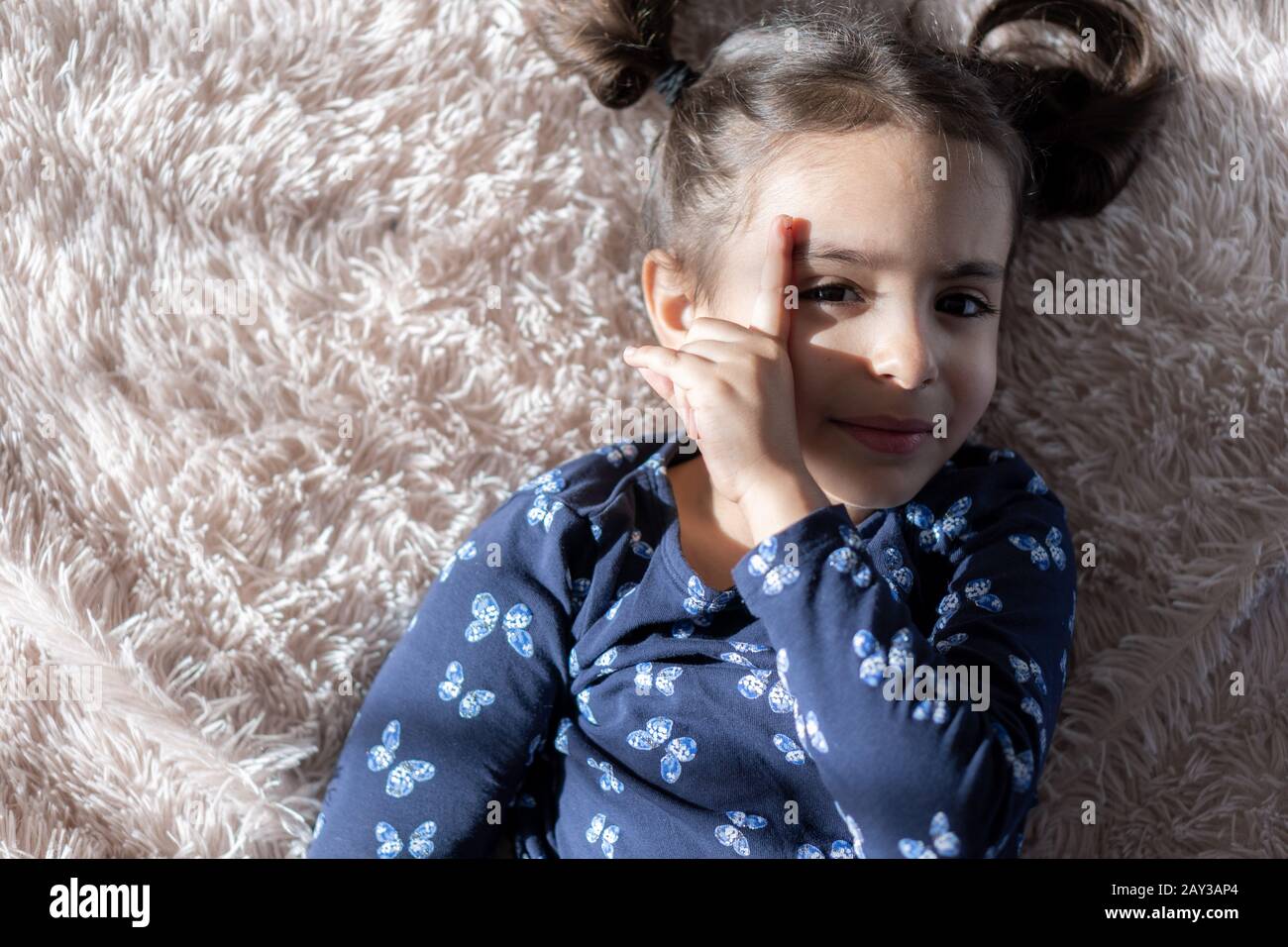 Middle Eastern young cute girl lies on a bright bed and closes her eyes with her finger from the sun. Persian swarthy girl on the bed. Middle Eastern Stock Photo